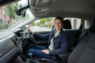 Femme souriante dans sa voiture en ville moderne